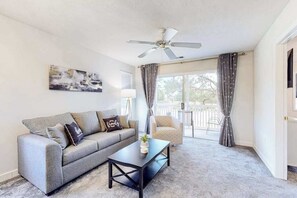 A living room with a sofa, coffee table, ceiling fan, and a view through a glass door to the outside. - River Oaks 40D 2BR Condo (Myrtle Beach)