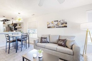 A modern living room with a grey sofa, a dining table with chairs, and a kitchen in the background. - River Oaks 40D 2BR Condo (Myrtle Beach)