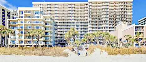 Un hotel frente al mar con varios pisos, balcones y palmeras.