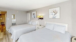Et hotelværelse med to senge, et sengebord, en lampe og et spejl.