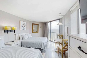 Ein Hotelzimmer mit zwei Betten, einem Schreibtisch, einem Stuhl, einem Esstisch und einem großen Fenster mit Blick.