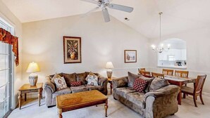 A living room with two sofas, a coffee table, a dining table with chairs, a ceiling fan, and a chandelier. - Cypress Bend Unit 434 (North Myrtle Beach)