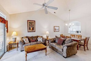 Ein Wohnzimmer mit zwei Sofas, einem Couchtisch, einem Esstisch mit Stühlen, einem Deckenventilator und einer Kristallleuchter.