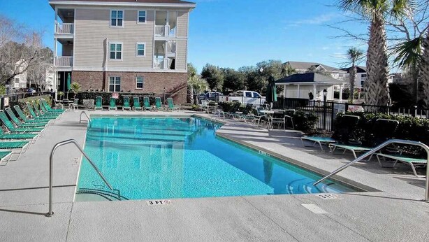 A swimming pool with lounge chairs, a building with multiple floors, and a clear sky. - Cypress Bend Unit 434 (North Myrtle Beach)