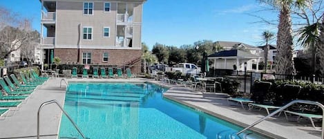 A swimming pool with lounge chairs, a building with multiple floors, and a clear sky.