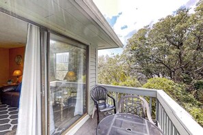 Ein Balkon mit Tisch und Stühlen, eine Schiebeglastür und Blick auf Bäume.