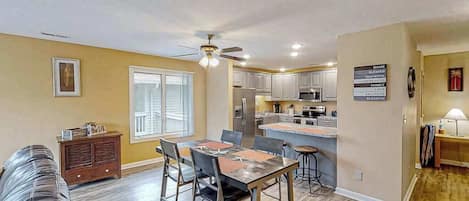 A spacious living room with a dining area, a kitchen, and a ceiling fan.