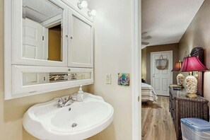 Un baño con lavamanos blanco, un espejo grande y una puerta que da a otra habitación.