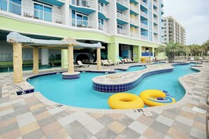 A hotel pool area with multiple swimming pools, lounge chairs, and a building with balconies. - Club Wyndham Unit 521 (North Myrtle Beach)