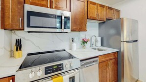 Una cocina con armarios de madera, microondas, estufa, lavavajillas y refrigerador.