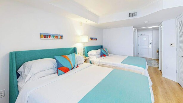 Habitación de hotel con dos camas, un ventilador de techo y una puerta que da a otra habitación.