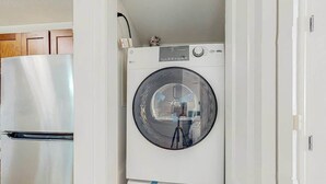 Un lavadero pequeño con lavadora de carga superior y refrigerador de acero inoxidable.