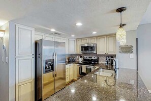 A modern kitchen with stainless steel appliances, granite countertops, and a hanging light fixture. - Shoreham Towers Unit 3-B (North Myrtle Beach)