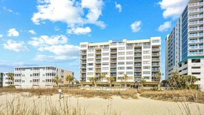 Et hotel ved stranden med flere etager, altaner og en sandstrand i forgrunden.