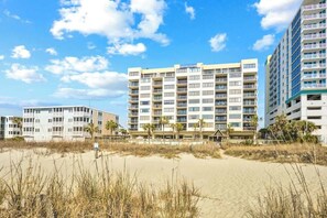 Ein Hotel direkt am Strand mit mehreren Etagen, Balkonen und einem Sandstrand im Vordergrund.