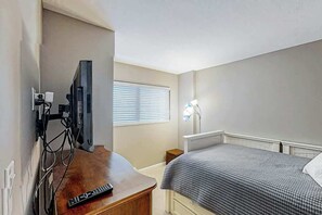 A hotel room with a bed, a desk with a remote control, a television, and a window with blinds. - Shoreham Towers Unit 3-B (North Myrtle Beach)