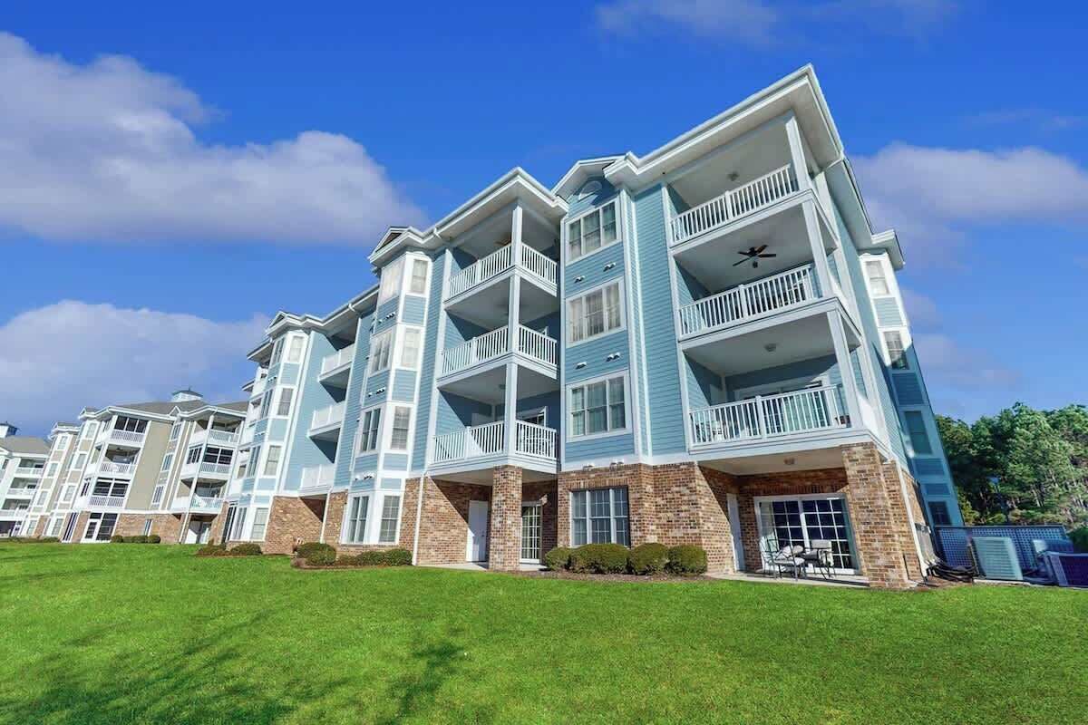 A multi-story residential building with balconies and a well-maintained lawn.