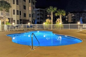 A swimming pool with a white fence, palm trees, and a building in the background. - Lakefront Waterview Retreat (Myrtle Beach)