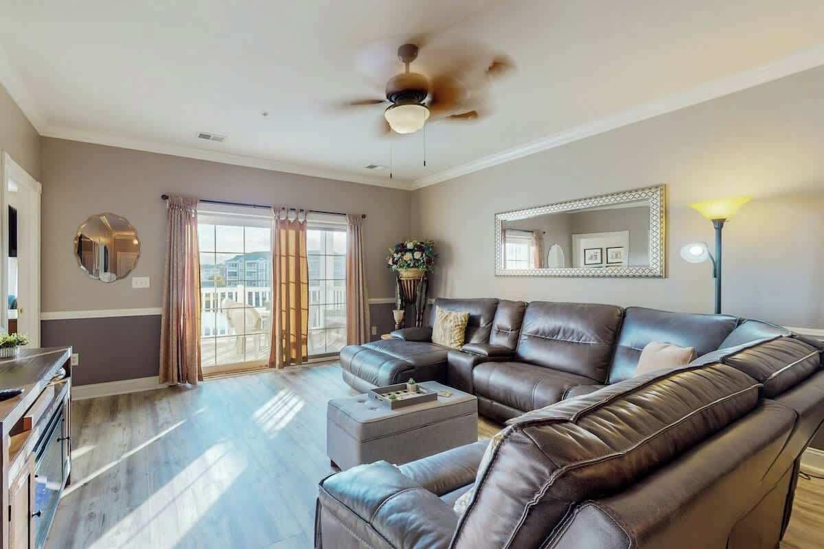Uma sala de estar ampla com um sofá seccional grande, um ventilador de teto e uma janela grande com cortinas.