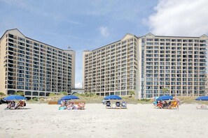 Ein Strandhotel mit mehreren Hochhäusern, Strandstühlen und Liegen.
