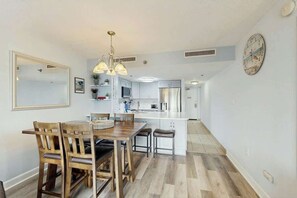 A modern kitchen with white cabinets, a central island, and a dining area with wooden chairs and a table. - Sunny and Ready Retreat (Myrtle Beach)