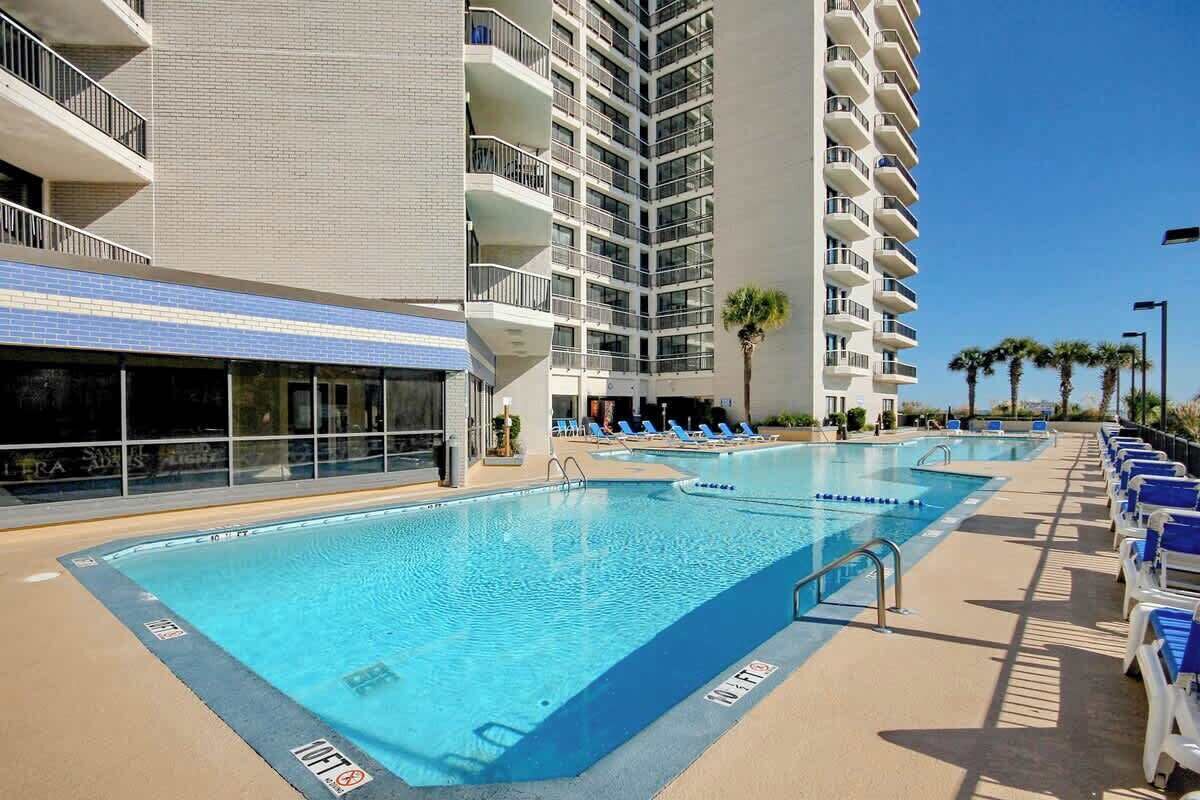 A pool area with lounge chairs and a building with multiple balconies.