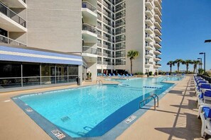 A pool area with lounge chairs and a building with multiple balconies. - Sunny and Ready Retreat (Myrtle Beach)