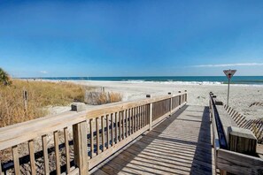 A wooden boardwalk leading to a beach with a warning sign. - Sunny and Ready Retreat (Myrtle Beach)
