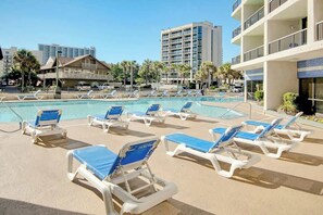 Zona de piscina amb gandules i un edifici al fons.