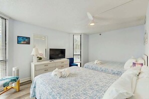 Ein Hotelzimmer mit zwei Betten, einem Fernseher, einem Schreibtisch und einem Deckenventilator.