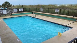 Ein rechteckiger Pool mit flacher Zone, umgeben von einem Metallzaun mit Warnschildern.
