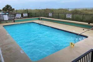 Ein rechteckiger Pool mit flacher Zone, umgeben von einem Metallzaun mit Warnschildern.