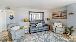 Ein Wohnzimmer mit grauem Sofa, zwei Sesseln, einem Couchtisch und einem gemusterten Teppich.