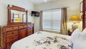 A bedroom with a bed, dresser, ceiling fan, TV, window with curtains, and a lamp. - Tupelo Bay, Unit 1514 (Murrells Inlet)