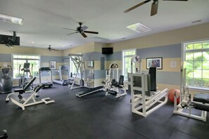 Ein Fitnessraum mit verschiedenen Trainingsgeräten, Deckenventilatoren und Fenstern.