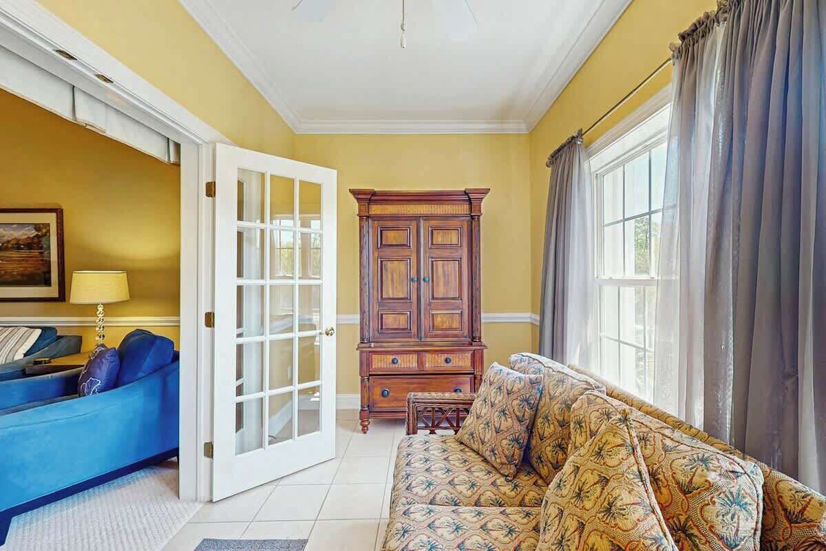 A room with a blue sofa, a patterned sofa, a wooden cabinet, and a large window with curtains.