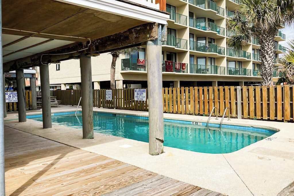A swimming pool area with a wooden deck, poolside chairs, and a wooden fence.