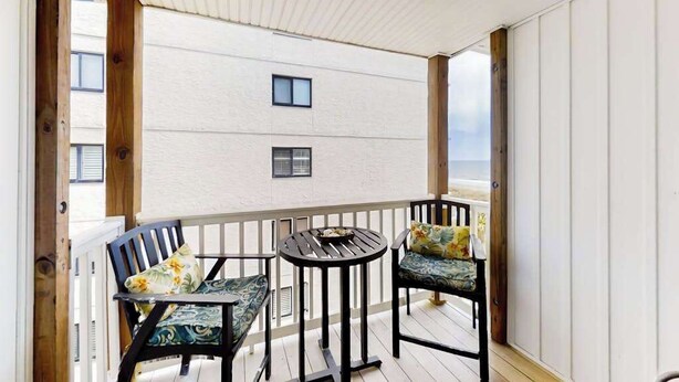 Ein Balkon mit Holzwertkasten, zwei Stühle mit Blumenkissen und ein kleiner runder Tisch.