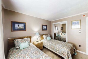 A bedroom with two beds, a nightstand, a mirror, and framed pictures on the wall. - Windy Village Unit C-2 (North Myrtle Beach)