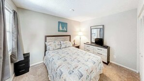 Ein Schlafzimmer mit Bett, Nachttisch, Lampe und Fernseher.