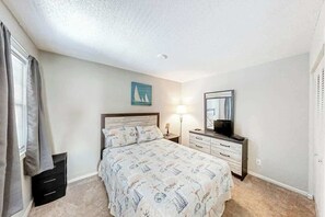 A bedroom with a bed, bedside table, lamp, and a television. - Ocean Greens Unit D-402 (North Myrtle Beach)