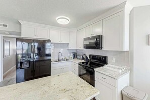 A modern kitchen with white cabinetry, stainless steel appliances, and a granite countertop. - Ocean Greens Unit D-402 (North Myrtle Beach)