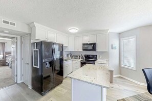 A modern kitchen with white cabinetry, stainless steel appliances, and a granite countertop. - Ocean Greens Unit D-402 (North Myrtle Beach)