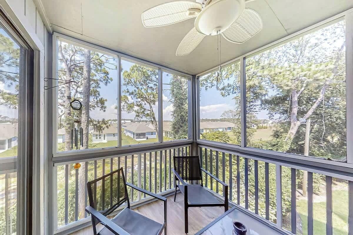 Ein Wintergarten mit Deckenventilator, großen Fenstern und Blick auf eine Wohngegend.