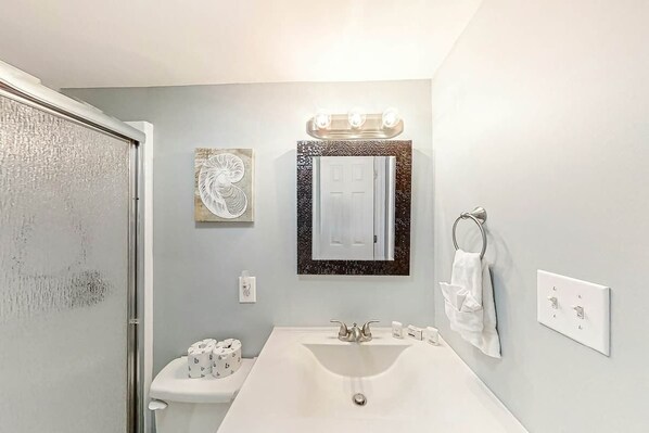 A bathroom with a white sink, a toilet, a mirror with lights, and a towel rack. - Ocean Greens Unit D-402 (North Myrtle Beach)
