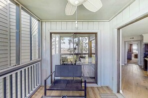 A covered porch with a bench, a ceiling fan, and a view of the backyard through glass doors. - Ocean Greens Unit D-402 (North Myrtle Beach)
