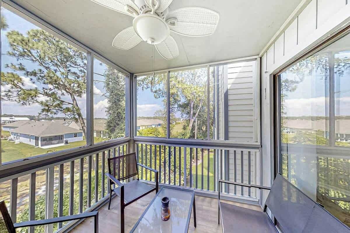 A sunlit balcony with a ceiling fan, a glass table, and a chair.