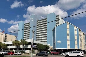 Ein Hotel mit mehreren Etagen und Balkonen, ein Parkplatz mit einigen Autos und ein klarer Himmel mit Wolken.