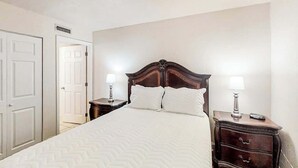A hotel room with a large bed, two bedside tables with lamps, a wardrobe, and a door to another room. - Water's Edge Resort 1002 (Murrells Inlet)
