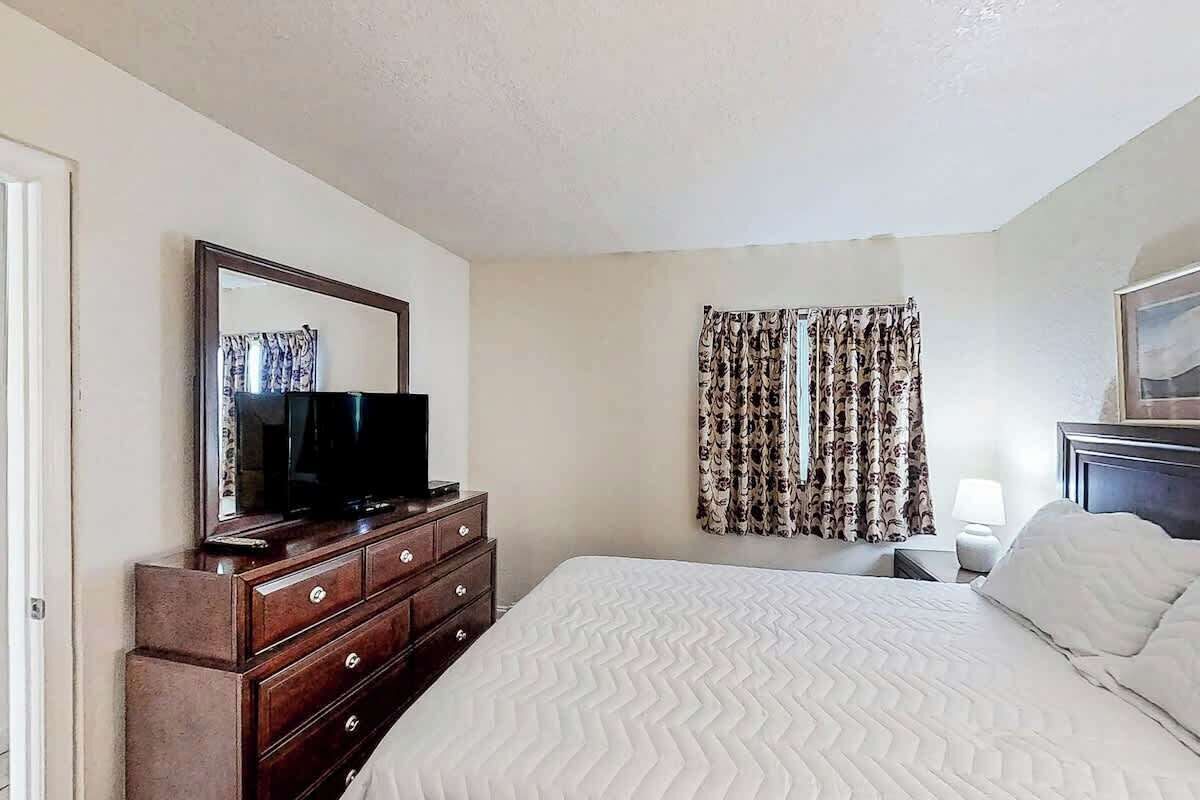 Um quarto com cama, cômoda, televisão e cortinas.
